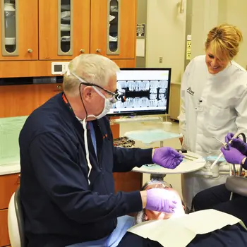 Dentist working on a patient while a dental assistant helps with procedure.