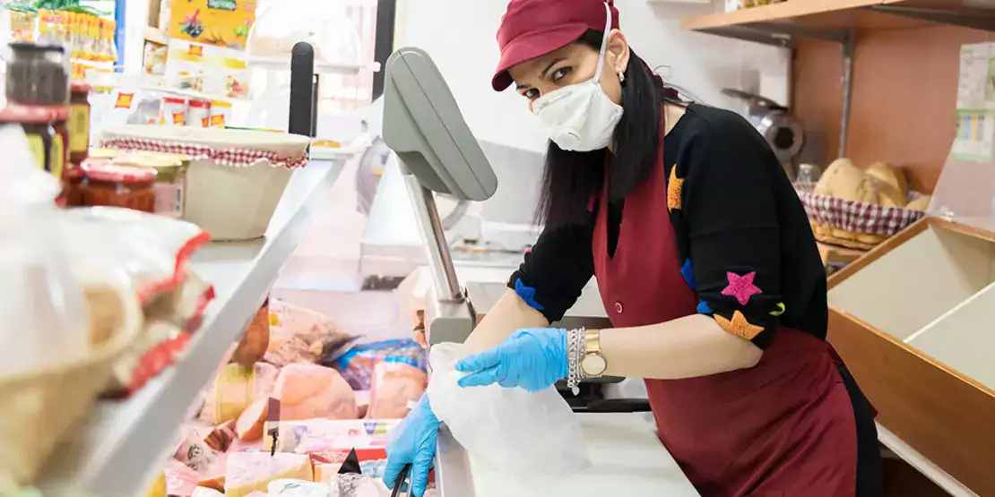 Woman behind food counter wearing gloves and mask