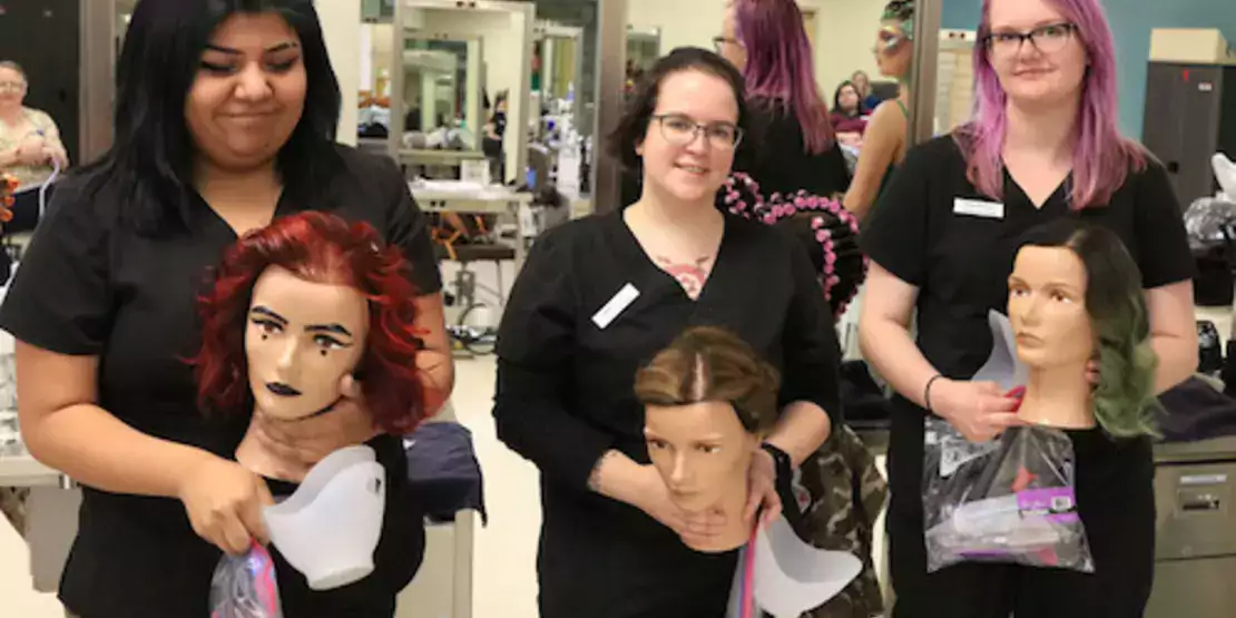 Cosmetology students holding mannequins