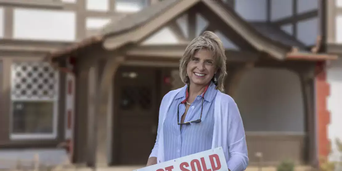 Anne Rasheed in front of a house holding a sold sign