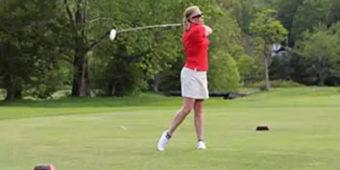 Female golfer wearing a red shirt, swinging her club.